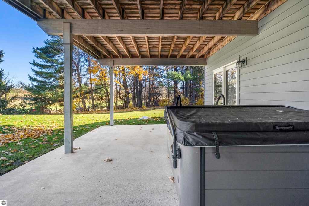 Covered patio area of a condo in Traverse City, featuring a hot tub, surrounded by mature trees and autumn foliage, providing a serene outdoor living space.
