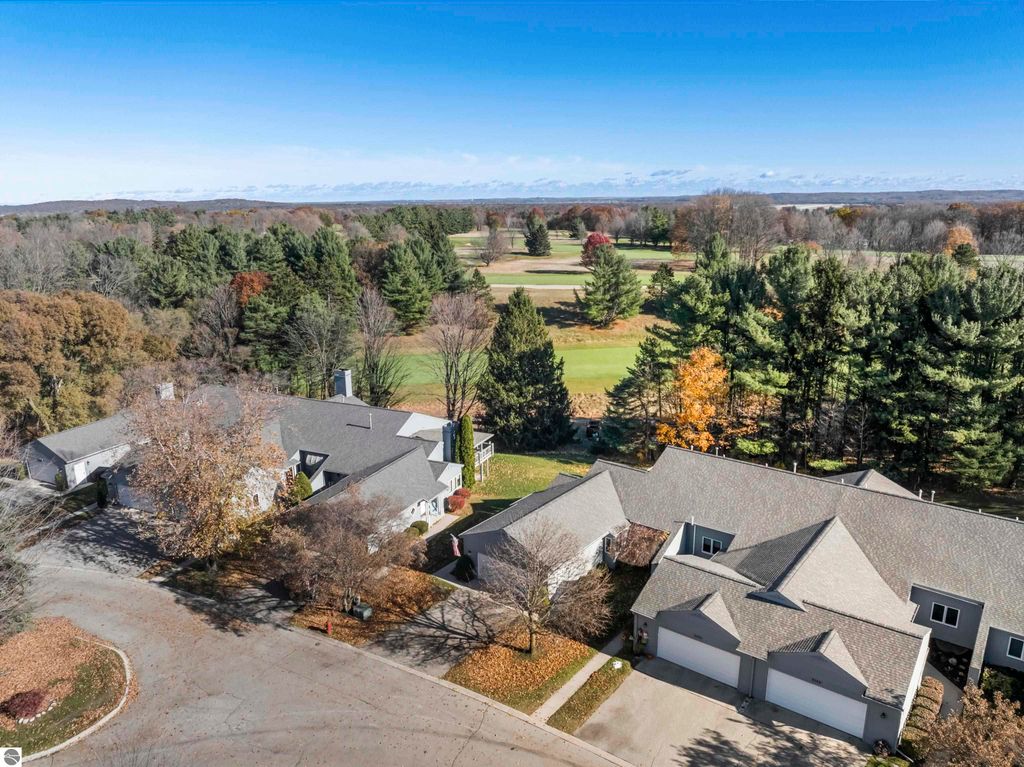 Aerial view of the Country Club Woods community in Traverse City, featuring well-maintained condos surrounded by mature trees and a golf course in the background.