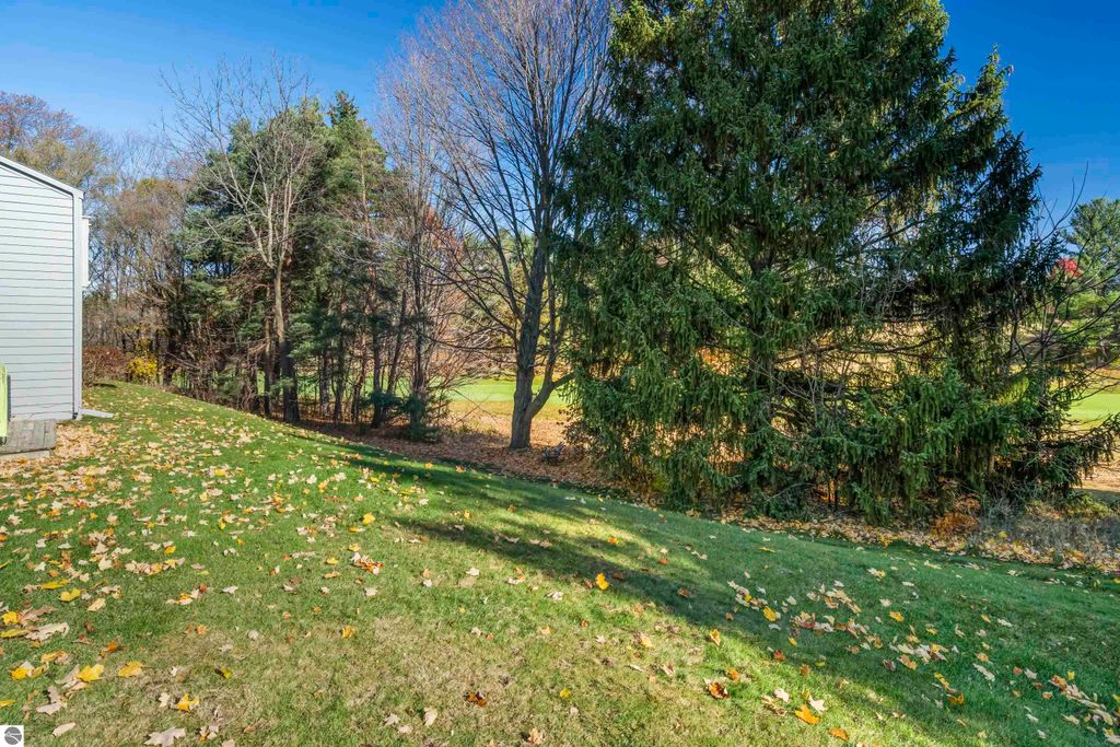 Scenic view of grassy yard with fallen leaves, mature trees, and golf course in background, showcasing the tranquil outdoor setting of the condo at 3756 Country Club Drive in Traverse City, MI.