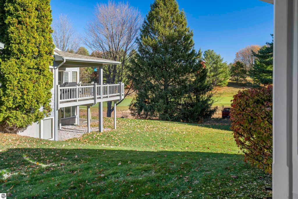 View of the exterior of a two-bedroom condo in Traverse City, featuring a balcony overlooking a golf course and surrounded by mature trees and landscaped grounds.