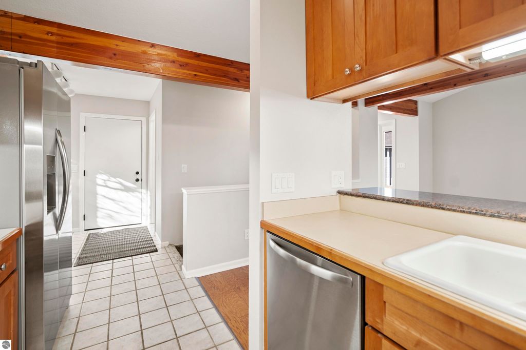 Updated kitchen interior with stainless steel appliances, granite countertops, and warm wood cabinetry, showcasing a welcoming entryway in the condo at 3756 Country Club Drive, Traverse City, MI.
