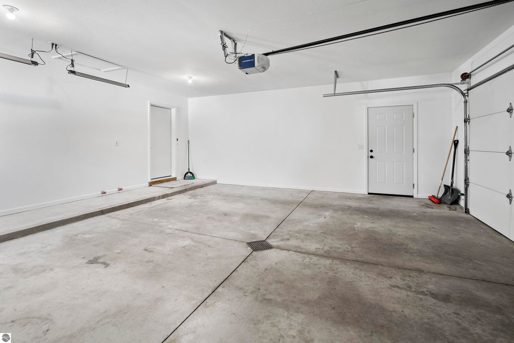 Spacious, clean garage interior with concrete flooring, white walls, and overhead storage, featuring a side door and garage door, suitable for the 2-bedroom condo at 3756 Country Club Drive in Traverse City, MI.