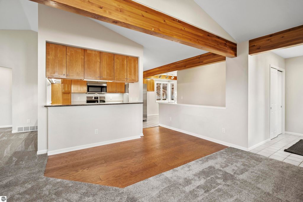 Interior view of a modern condo showcasing an open floor plan with wood beams, kitchen cabinetry, and a cozy living area, reflecting the updated features of the 2-bedroom, 2-bath condo for sale in Traverse City, MI.