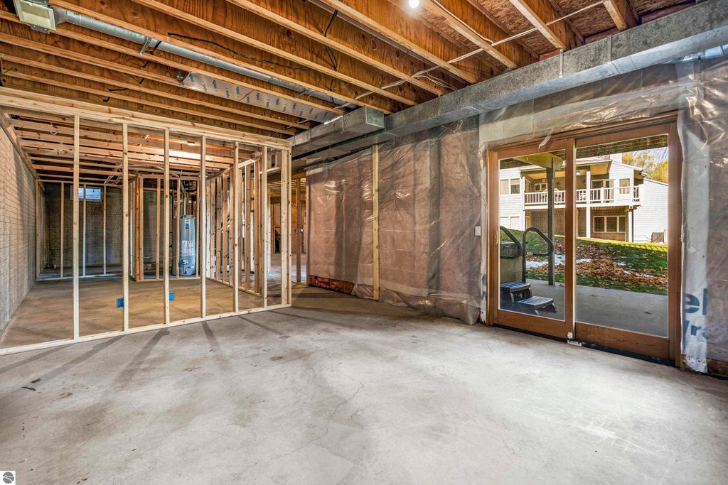 Unfinished lower level of a condo in Traverse City, showcasing framed walls, exposed beams, and a walkout patio door leading to a serene outdoor view, highlighting potential for customization and additional living space.