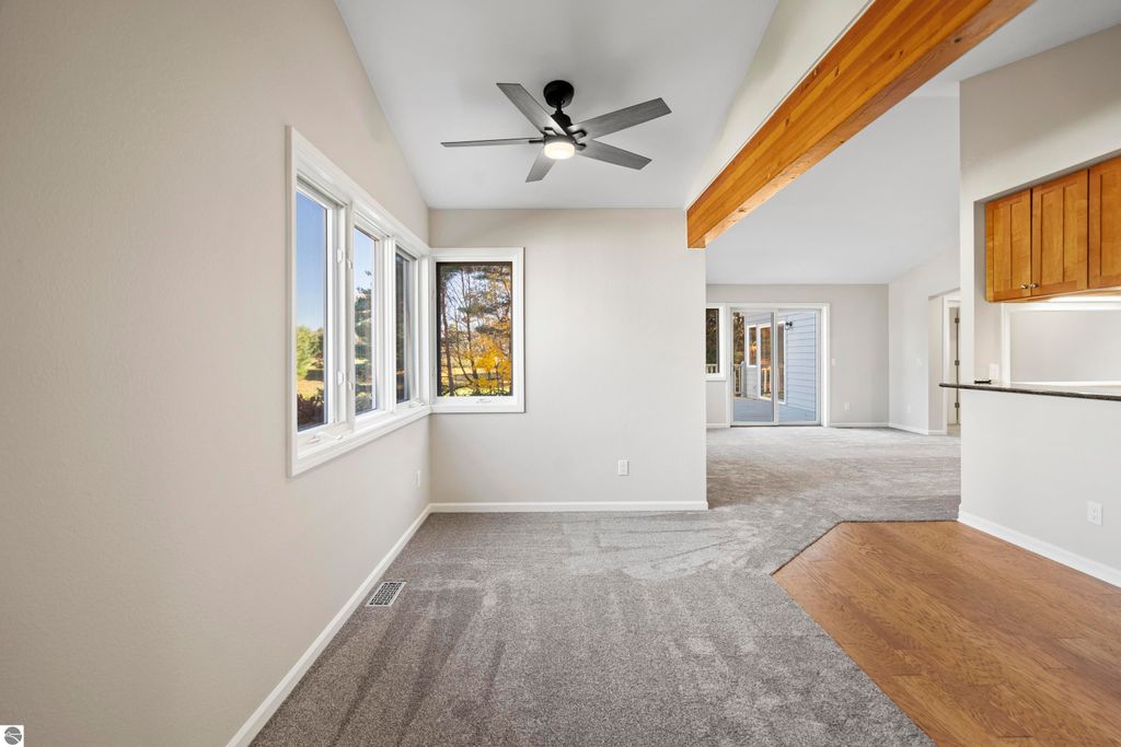 Light-filled interior of a condo at 3756 Country Club Drive, featuring new carpeting, large windows, and a ceiling fan, with a view of mature trees and golf course beyond.