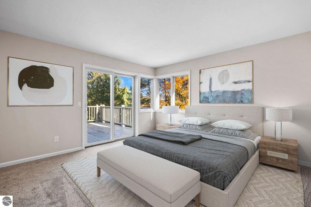 Bright and modern bedroom with a cozy bed, large windows showcasing autumn foliage, and contemporary artwork, highlighting the tranquil living space of the condo at 3756 Country Club Drive in Traverse City.