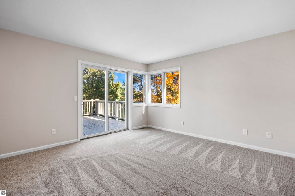 Light-filled living room in a 2-bedroom condo at 3756 Country Club Drive, featuring large windows, sliding glass doors to a balcony, and new carpet, overlooking mature trees and a golf course.