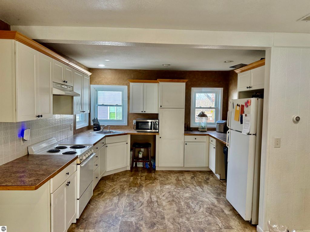 Spacious open kitchen with white cabinetry, modern appliances, and natural light from windows, ideal for gatherings in a property listed at 711 Francisco Avenue, Alma, MI.