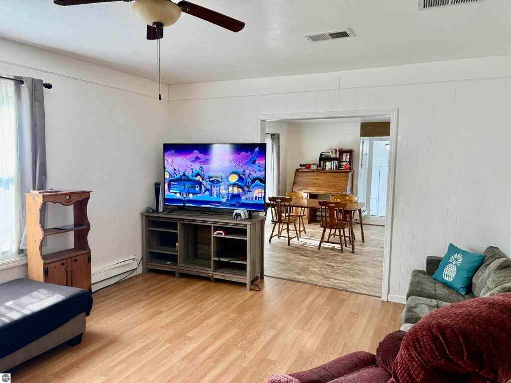 Living room with a TV displaying animated content, featuring a sofa, wooden shelving unit, and a view into the dining area with a table and chairs, showcasing the spacious interior of the investment property at 711 Francisco Avenue, Alma, MI.