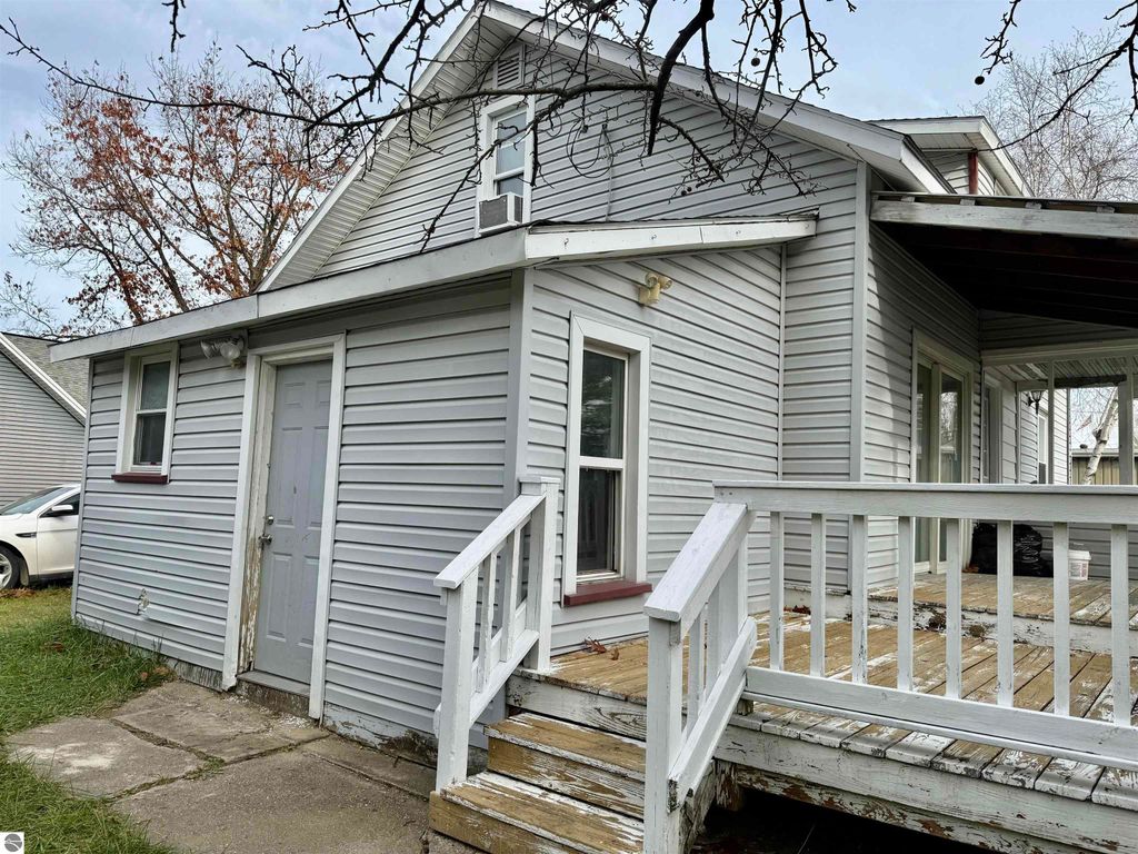 Exterior view of a single-family home at 711 Francisco Avenue, Alma, MI, featuring a porch, grey siding, and a side entrance, suitable for investment property listing.