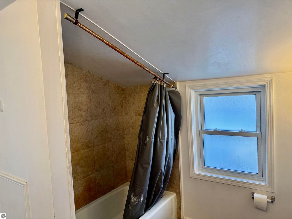 Bathroom interior featuring a bathtub, gray shower curtain, tiled walls, and a window providing natural light.