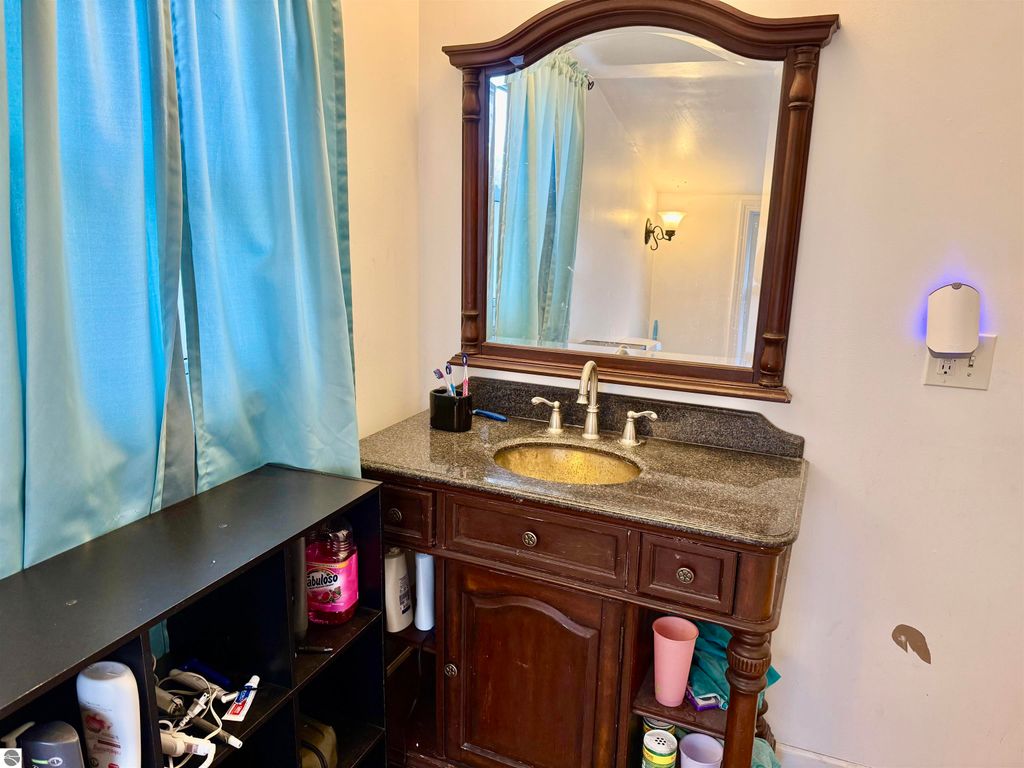 Bathroom vanity with a mirror, blue curtains, and storage shelf, featuring a granite countertop and sink, ideal for the property at 711 Francisco Avenue, Alma, MI.