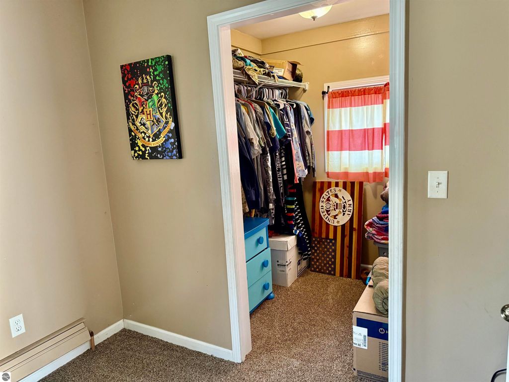 Bedroom closet with organized clothing, blue storage drawers, and a Harry Potter-themed artwork on the wall, featuring a window with red and white striped curtains.