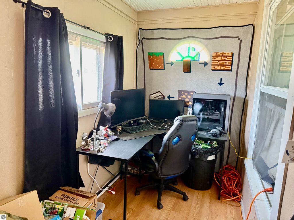 Home office setup with dual monitors, gaming chair, and a Minecraft-themed blanket on the wall, surrounded by storage boxes and cables.