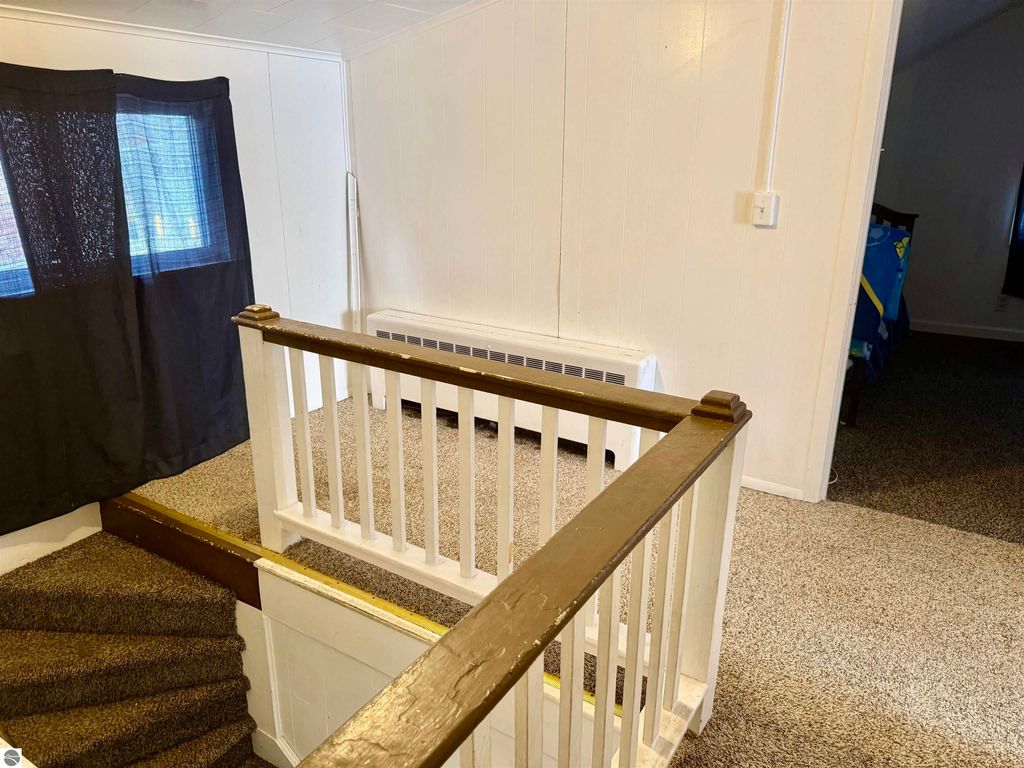Interior view of the staircase and landing area in a rental property at 711 Francisco Avenue, featuring carpeted flooring, a wooden banister, and a window with black curtains.