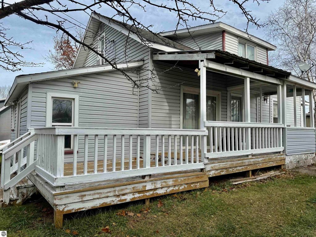 Exterior view of the house at 711 Francisco Avenue, Alma, MI, featuring a porch with railing, gray siding, and a well-maintained yard, showcasing its potential as an investment property.