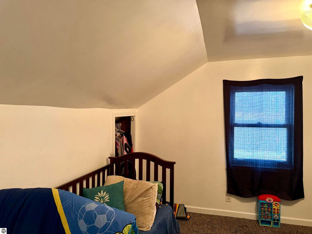 Cozy bedroom with sloped ceiling, featuring a crib, colorful bedding, and a window with blue curtains, suitable for a child or as a rental space in the property at 711 Francisco Avenue, Alma, MI.