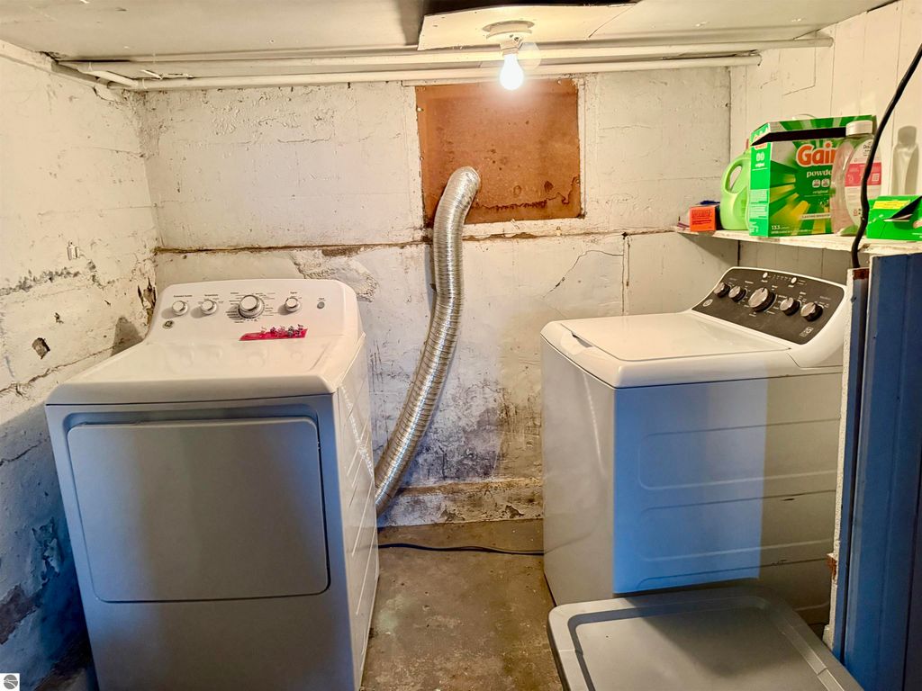 Laundry room featuring two washing machines, exposed brick walls, and storage for laundry supplies, relevant to the property listing at 711 Francisco Avenue, Alma, MI.