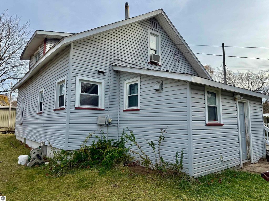 Exterior view of a two-story residential home at 711 Francisco Avenue, Alma, MI, featuring gray siding, multiple windows, and a side entrance, surrounded by a grassy yard and utility connections, relevant to investment property listing.