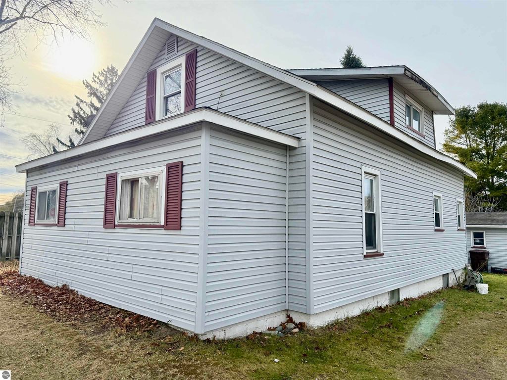 Exterior view of 711 Francisco Avenue, Alma, MI, showcasing the house's siding, windows with maroon shutters, and surrounding yard space, highlighting its potential as an investment property.