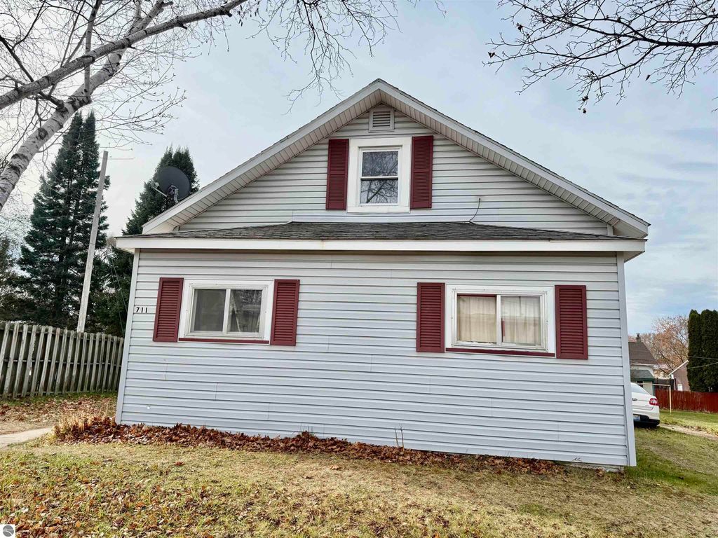 House exterior at 711 Francisco Avenue, Alma, MI, featuring a light blue facade, red shutters, and a sloped roof, surrounded by grass and trees, highlighting its potential as an investment property.