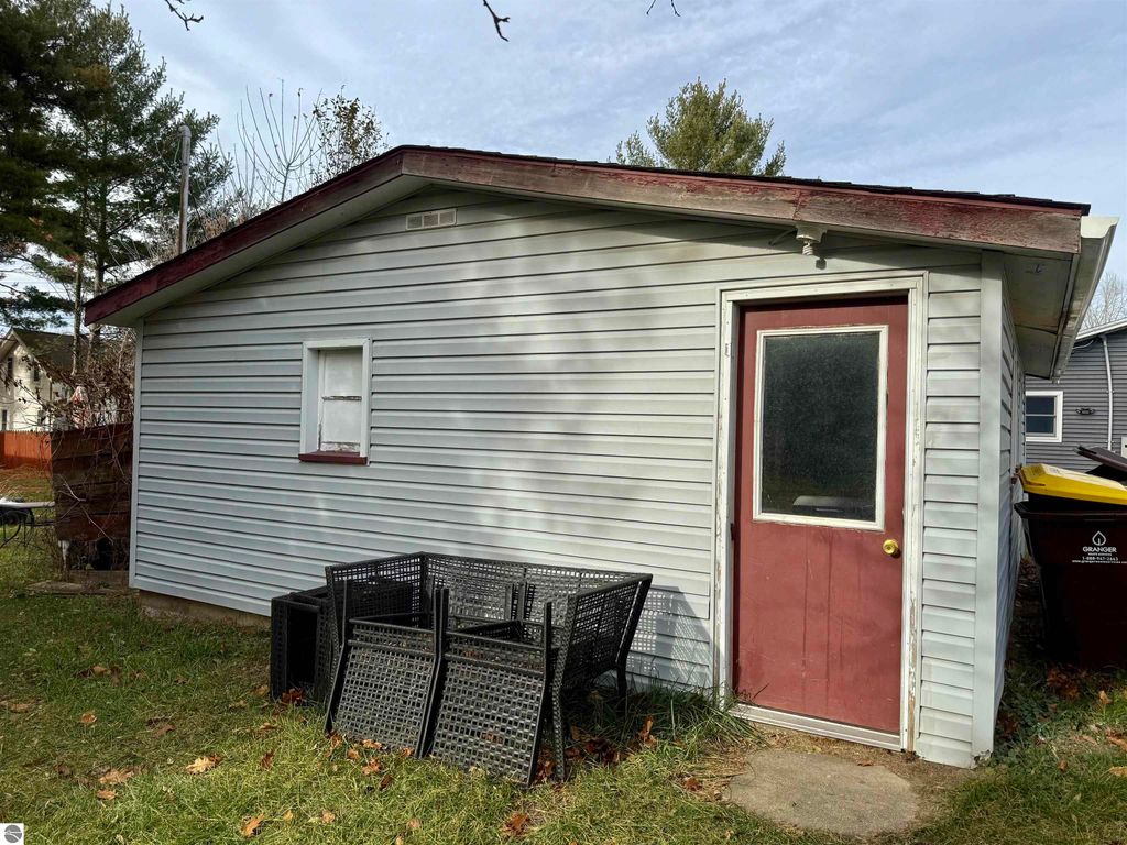 Exterior view of a storage outbuilding with a red door, surrounded by grass and outdoor furniture, located at 711 Francisco Avenue, Alma, MI, suitable for additional storage or recreational space.