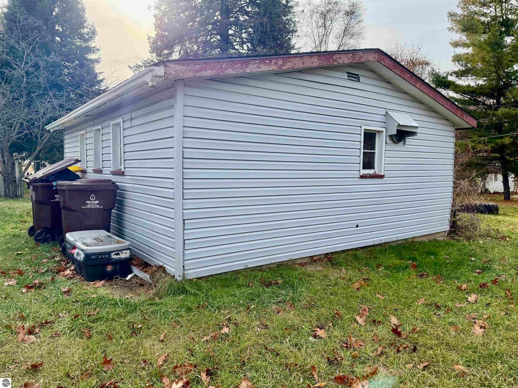 Exterior view of the home at 711 Francisco Avenue, Alma, MI, showing the side with windows, a sloped roof, and trash bins in the yard, highlighting its potential as an investment property.
