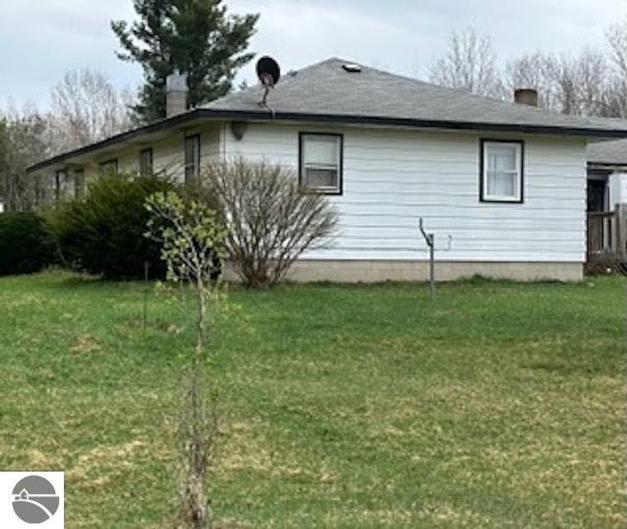 Single-family home at 4419 10 Mile Road, Evart, MI, featuring a white exterior, surrounded by greenery, showcasing a large yard and nearby trees, ideal for country living on a 14.5-acre lot.