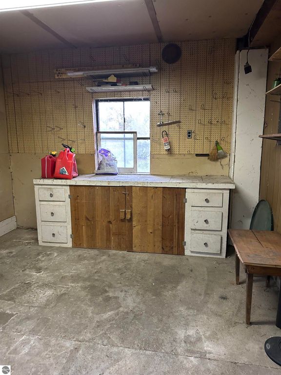 Interior view of a workshop area featuring a wooden workbench with drawers, a window providing natural light, and various storage items, illustrating potential for a workshop or gardening shed in a home listing for 4419 10 Mile Road, Evart, MI.