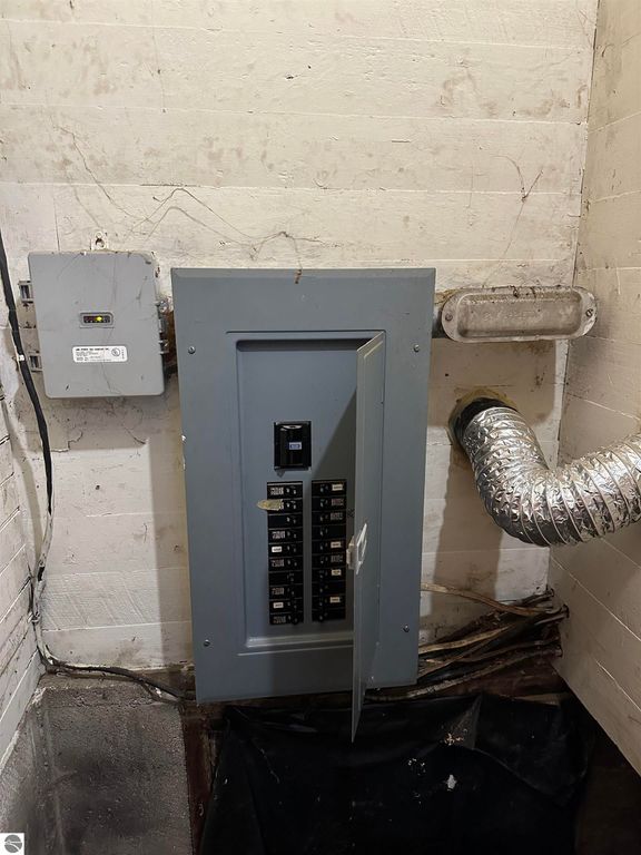 Electrical panel with circuit breakers and vent duct in a basement setting.