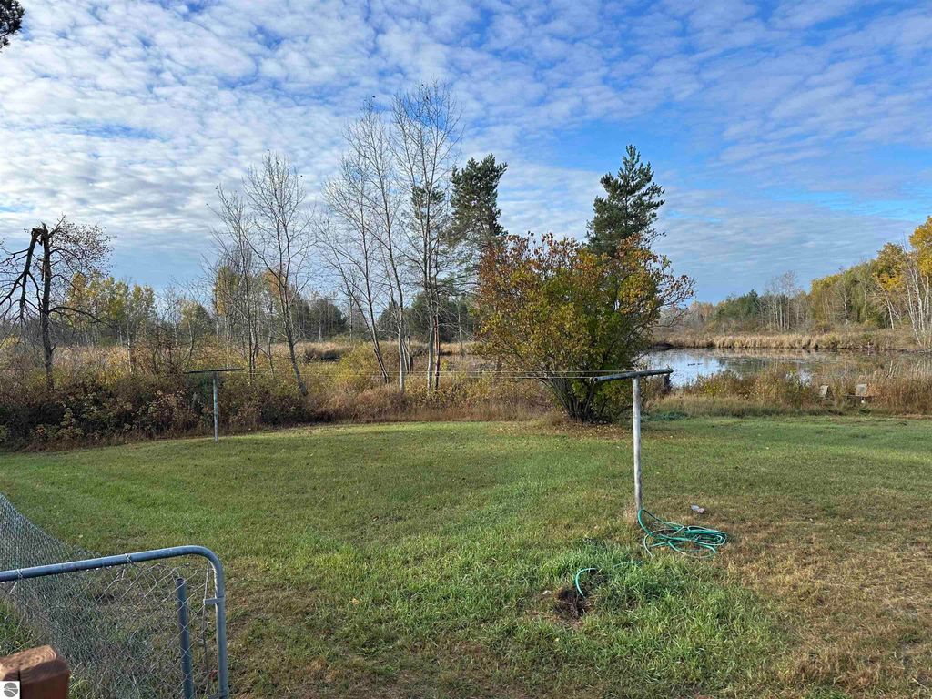 Backyard view of a home in Evart, MI, featuring a grassy area, trees, and a pond, highlighting the property's natural surroundings on 14.5 acres.