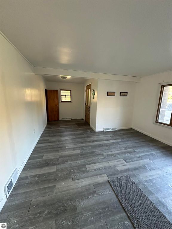 Interior view of a living space in a 3-bedroom home for sale at 4419 10 Mile Road, Evart, MI, featuring gray laminate flooring, natural light from a window, and adjacent doorways.