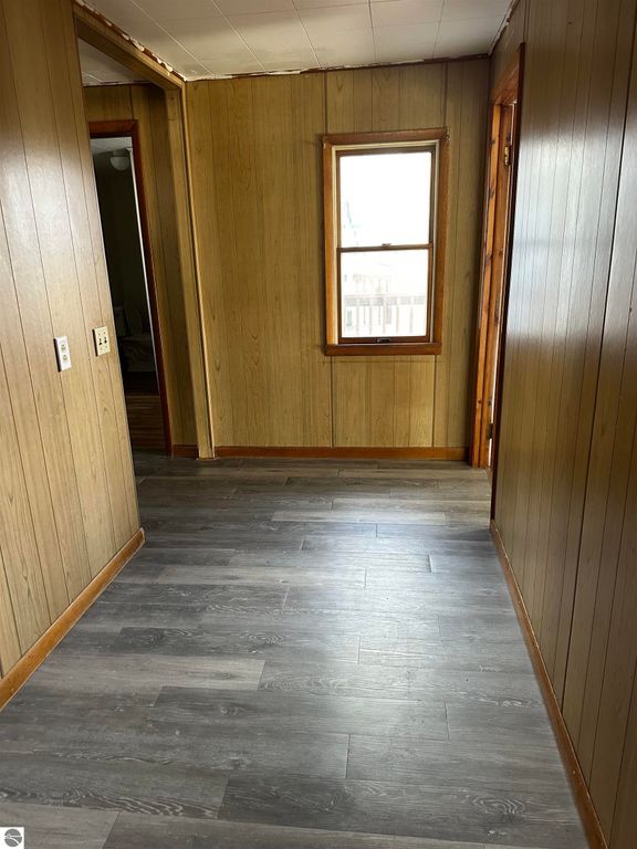 Interior hallway of a home with wooden paneling, gray flooring, and a window providing natural light, showcasing the layout of the property for sale at 4419 10 Mile Road, Evart, MI.
