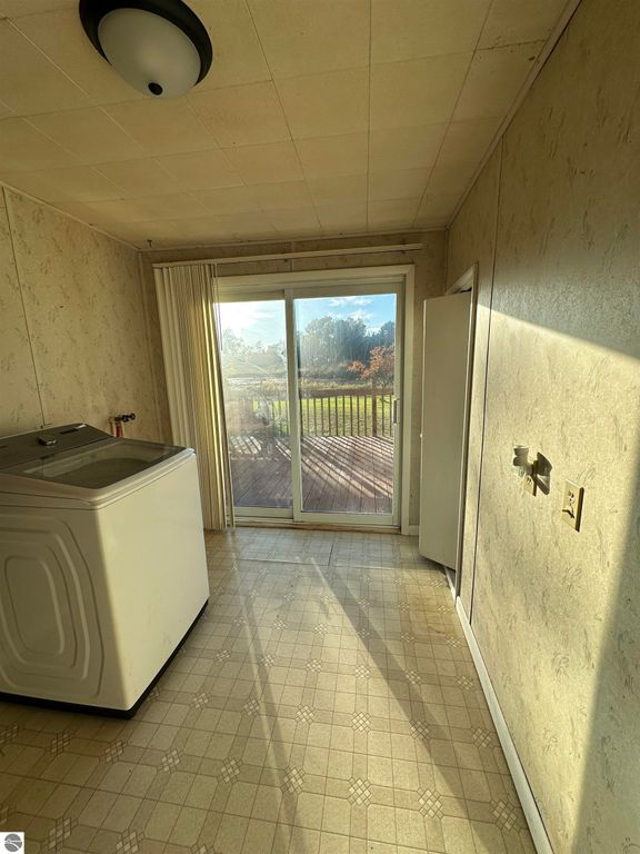 Laundry room with washing machine, sliding glass door leading to outdoor deck, natural light illuminating space, and neutral wall colors, suitable for family home at 4419 10 Mile Road, Evart, MI.