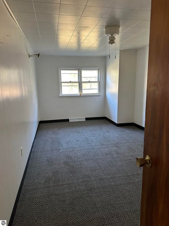 Empty room with carpeted floor, white walls, and a ceiling fan, featuring a window for natural light, part of the 3-bedroom home at 4419 10 Mile Road, Evart, MI.