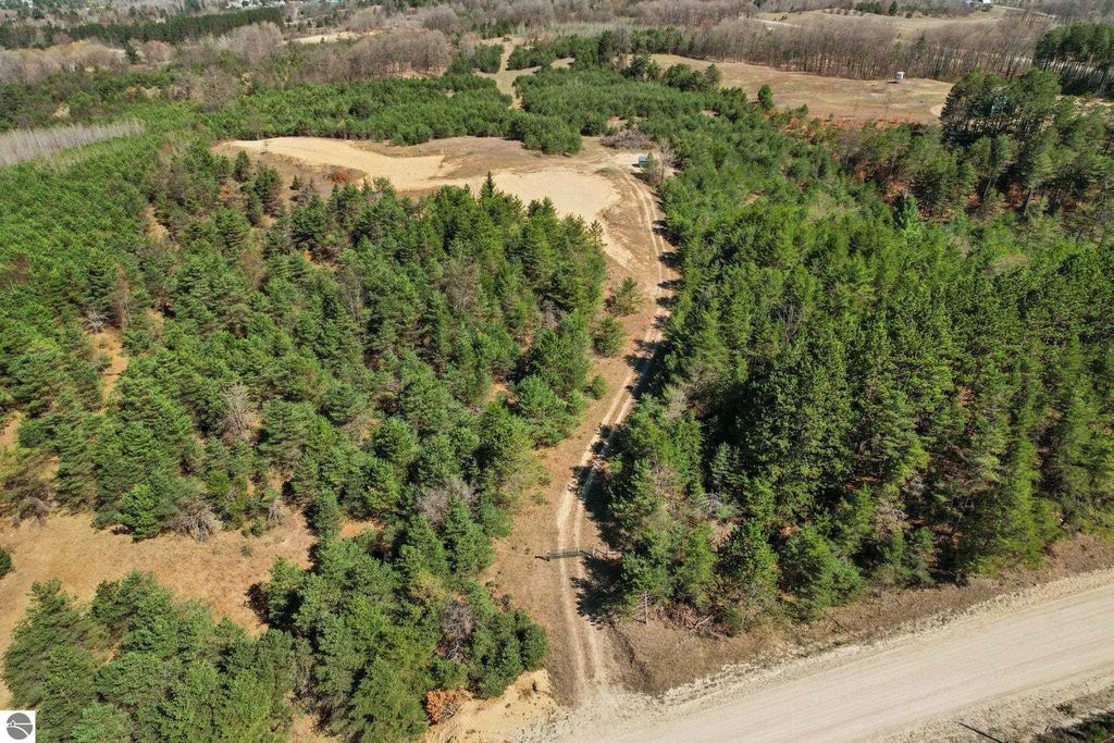 Aerial view of a 7.62-acre wooded parcel in Manton, MI, featuring dense trees, open areas, and a dirt access road, ideal for outdoor activities and privacy.