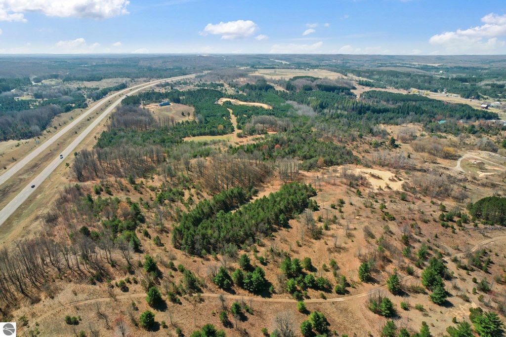 Aerial view of 7.62-acre land parcel in Manton, MI, showcasing wooded areas and proximity to highway, ideal for outdoor activities and privacy.