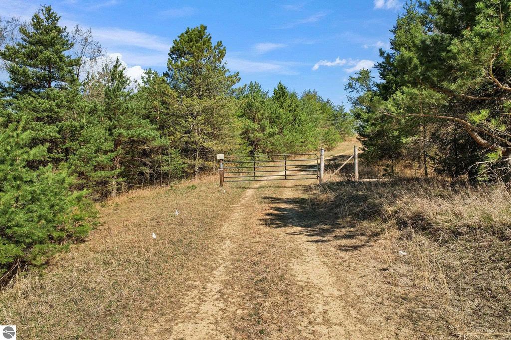 Gated entrance along a dirt road surrounded by trees, leading to a 7.62-acre parcel of land for sale in Manton, MI, ideal for outdoor activities and privacy.
