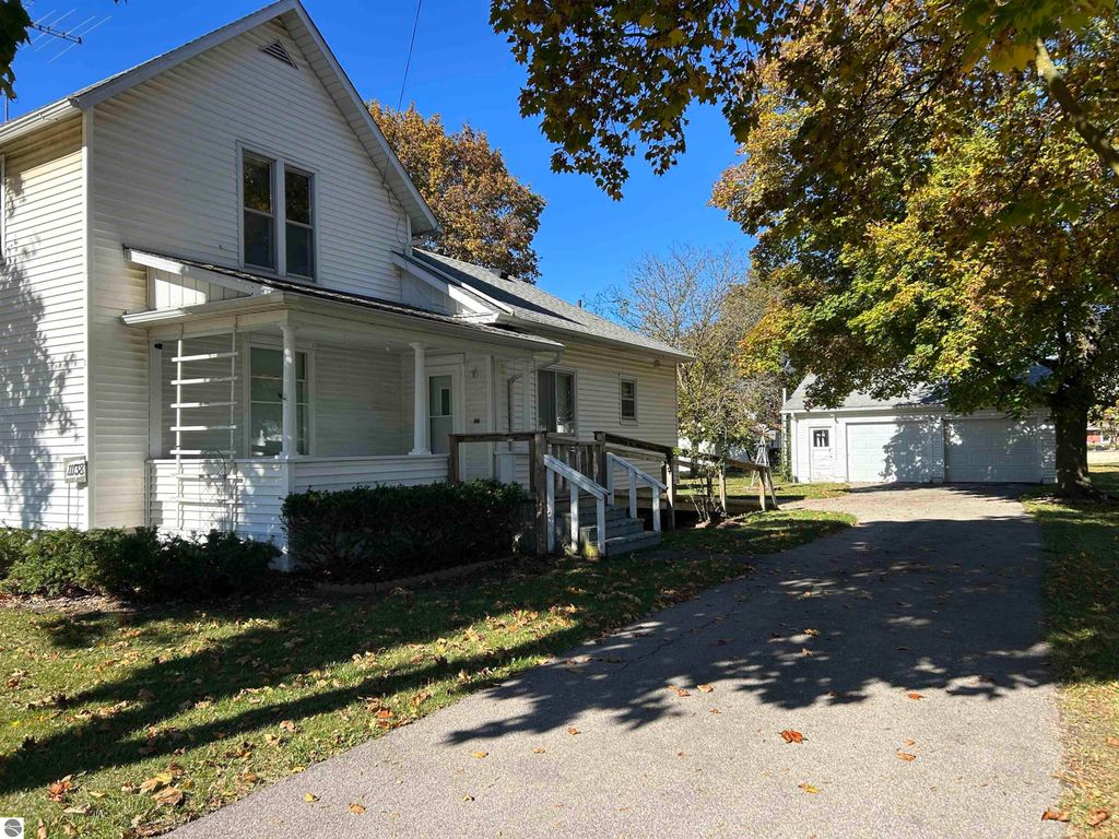 Two-story white house with front porch, surrounded by trees and a driveway leading to a detached garage, located at 11138 W 2nd Street, Fowler, MI.