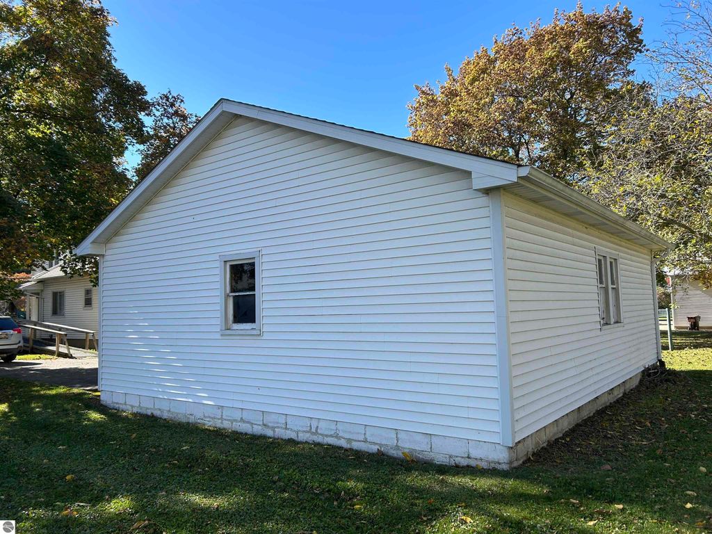 Side view of a white house at 11138 W 2nd Street, Fowler, MI, showcasing the exterior siding, windows, and surrounding greenery.