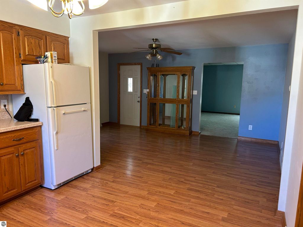 Open kitchen with wooden cabinets and white refrigerator, leading to a spacious living area in a 4-bedroom home at 11138 W 2nd Street, Fowler, MI.