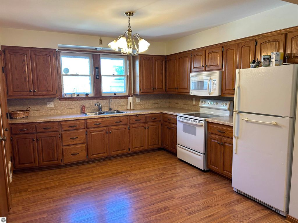 Kitchen with wooden cabinets, white appliances, and a large window, showcasing a spacious layout suitable for family gatherings in the Fowler, MI home listing.