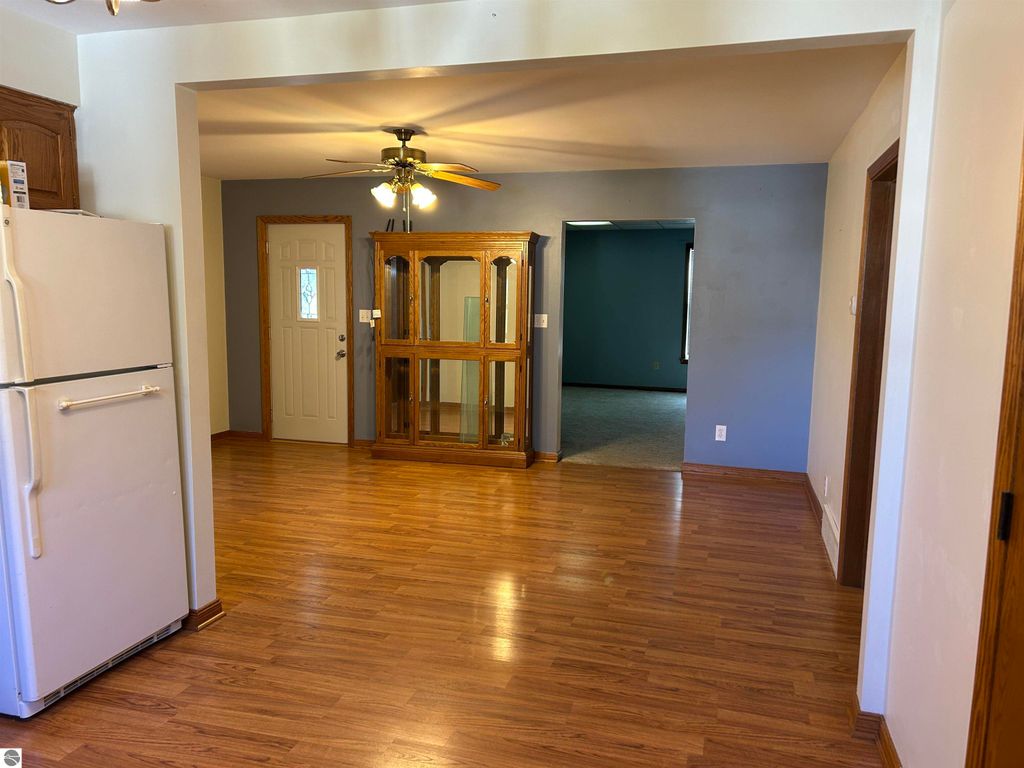 Interior view of a home at 11138 W 2nd Street, Fowler, MI, featuring an open kitchen with a refrigerator, hardwood flooring, a door leading outside, and a wooden display cabinet, highlighting the spacious layout suitable for family gatherings.