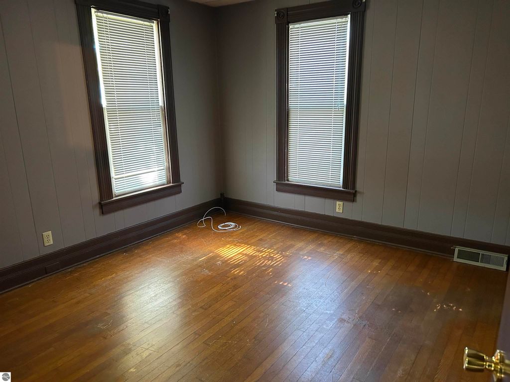 Empty room with hardwood floors, two windows with blinds, and gray walls, showcasing potential for a bedroom or office space in the Fowler home listing.