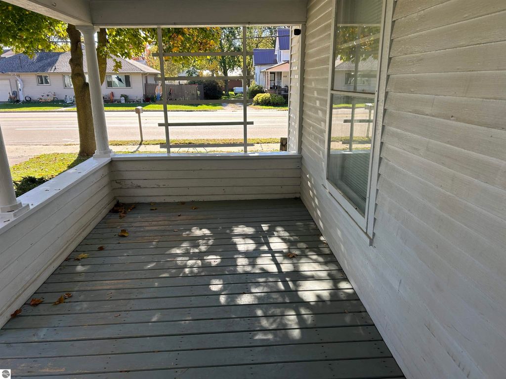 Front porch of a home at 11138 W 2nd Street, Fowler, MI, featuring wooden flooring, white railings, and natural light casting shadows, with a view of the street and nearby houses.