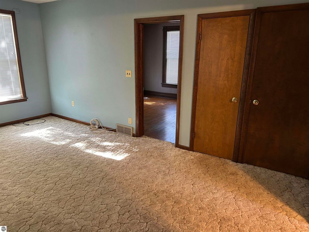 Interior view of a living room in a 4-bedroom home for sale at 11138 W 2nd Street, Fowler, MI, featuring beige carpet, light blue walls, and a doorway leading to another room with hardwood flooring.