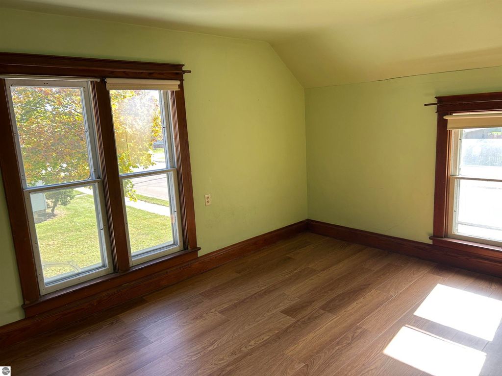 Interior view of a bedroom in a home at 11138 W 2nd Street, Fowler, MI, featuring two large windows, light green walls, and hardwood flooring, showcasing natural light and potential for personalization.