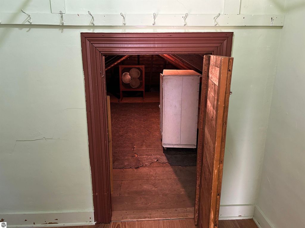 Attic entrance with wooden door, revealing spacious storage area, fan, and white cabinet, in a home located at 11138 W 2nd Street, Fowler, MI.