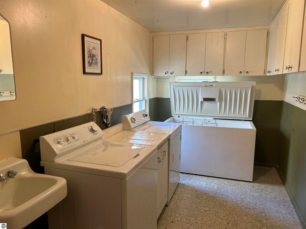 Laundry room with washer, dryer, and deep freezer, featuring ample storage cabinets and a sink, suitable for a family home in Fowler, MI.