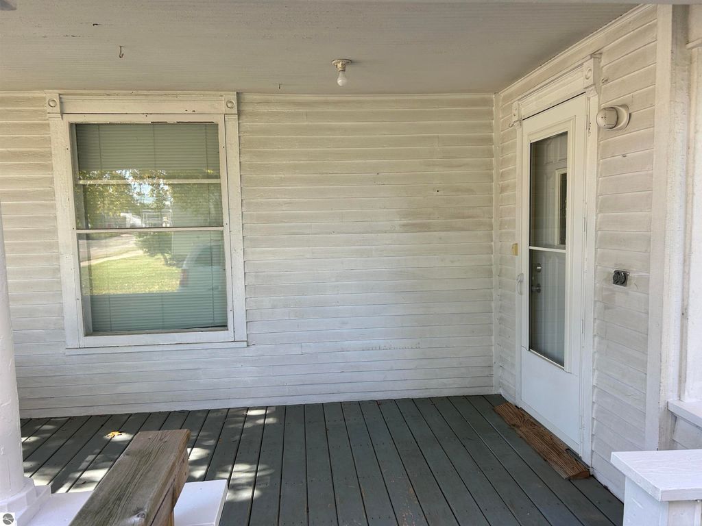 Front porch entrance of a home at 11138 W 2nd Street, Fowler, MI, featuring white wooden siding, a partially visible door, and a window with blinds, showcasing a welcoming outdoor space.